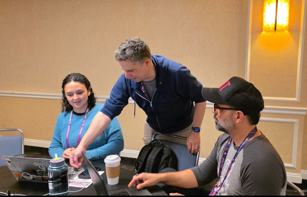 Three contributors collaborating around laptops at a pyOpenSci development sprint